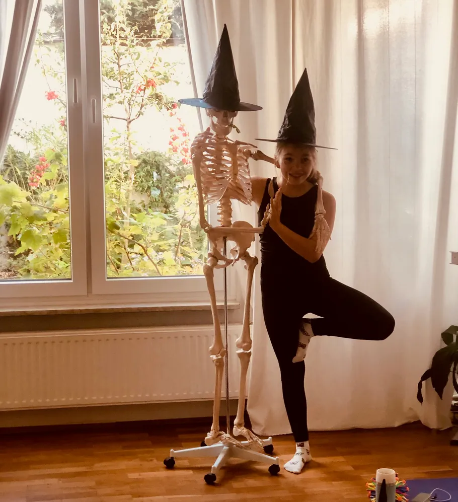 Person and skeleton wearing witch hats indoors.