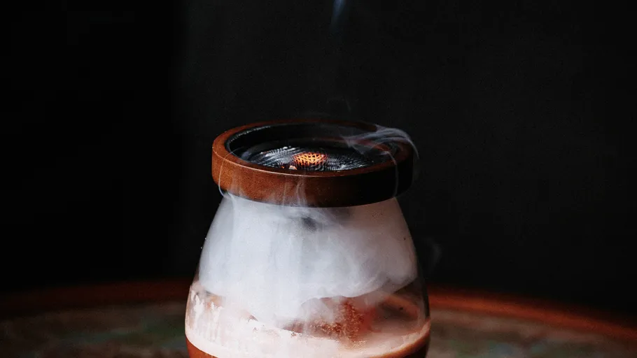 Steaming glass beverage smoker on table.