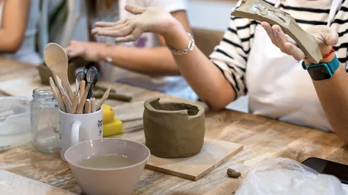 Person sculpting clay pot on table.