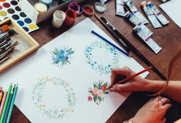 Person drawing floral designs on paper.