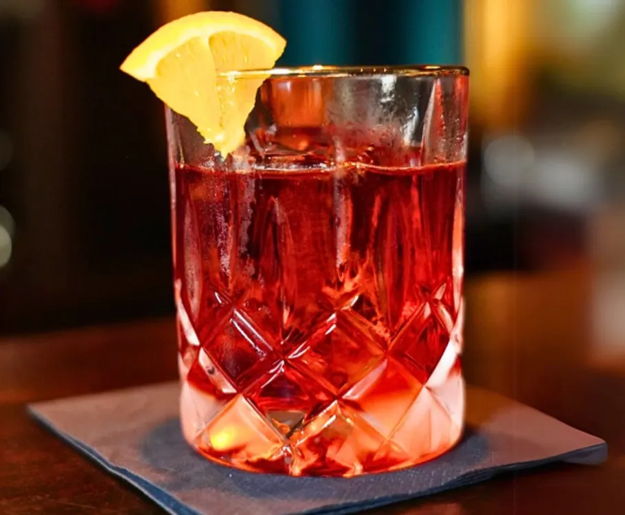 Red cocktail with orange slice garnish.