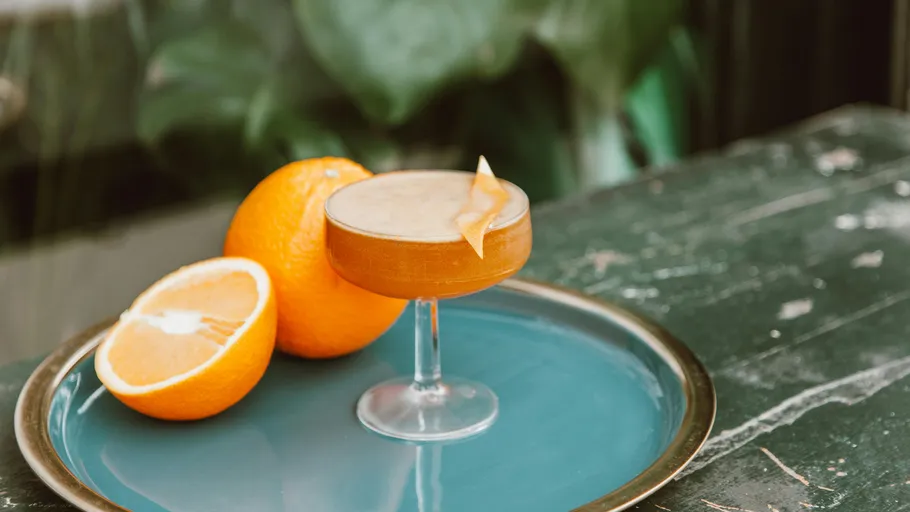 Cocktailglas mit Orangengarnitur auf Tablett.