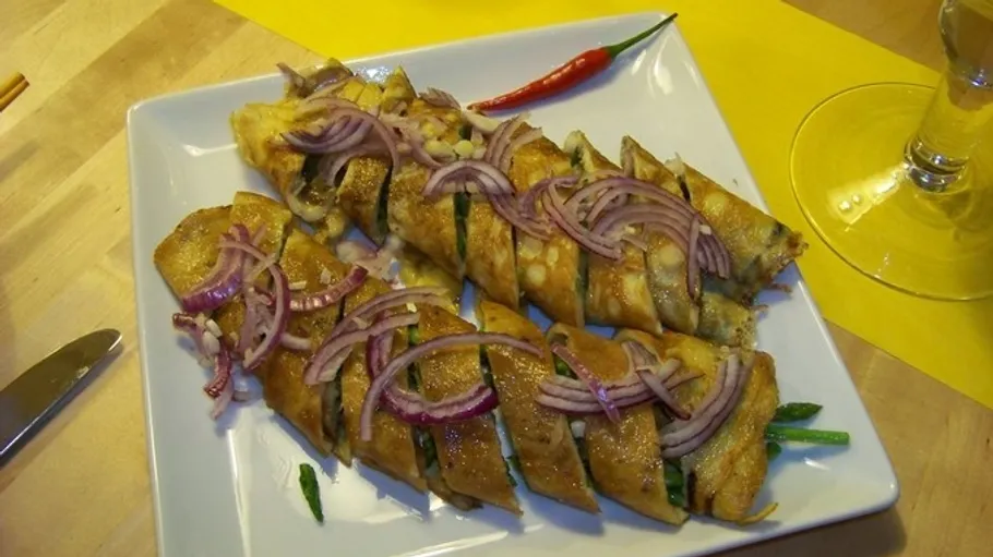 Rolled crepes with red onion on plate.