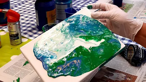 Hand tilts paint-covered canvas on table.