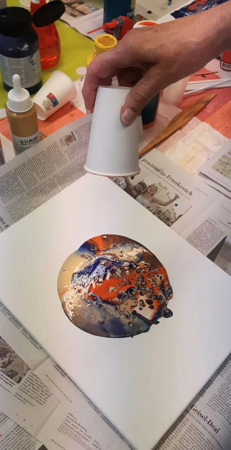 Hand lifting cup above colorful paint pour.