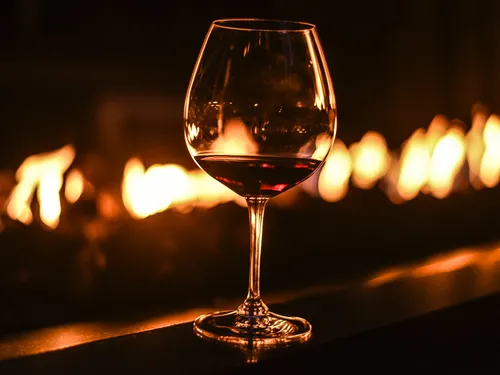 Rotwein-Glas steht vor einem flackernden Feuer.