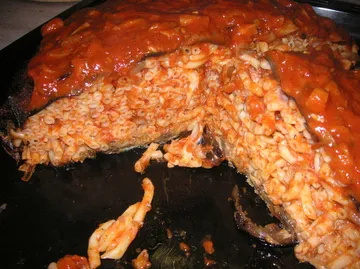 Nudelauflauf mit roter Soße auf schwarzem Blech.