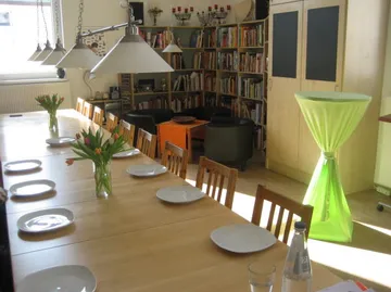 Set dining table in bright room, bookshelves nearby.