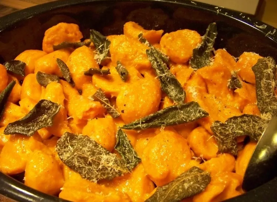 Orange gnocchi with sage in a black bowl.