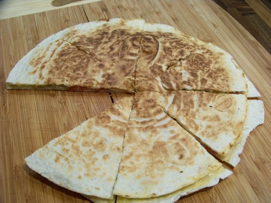 Sliced quesadilla on wooden cutting board.