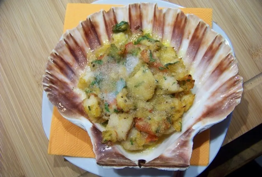 Überbackenes Meeresfrüchtegericht in großer Muschelschale.