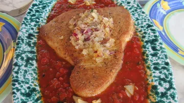 Gekochter Fisch auf Tomatensauce mit Zwiebeln.