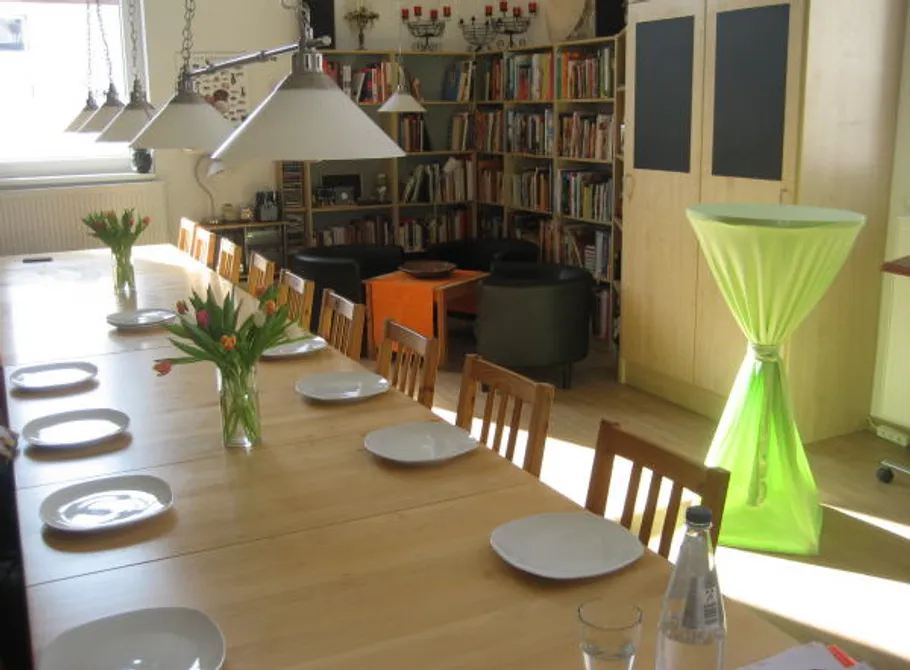 Dining table set with plates, flowers, bookshelf nearby.