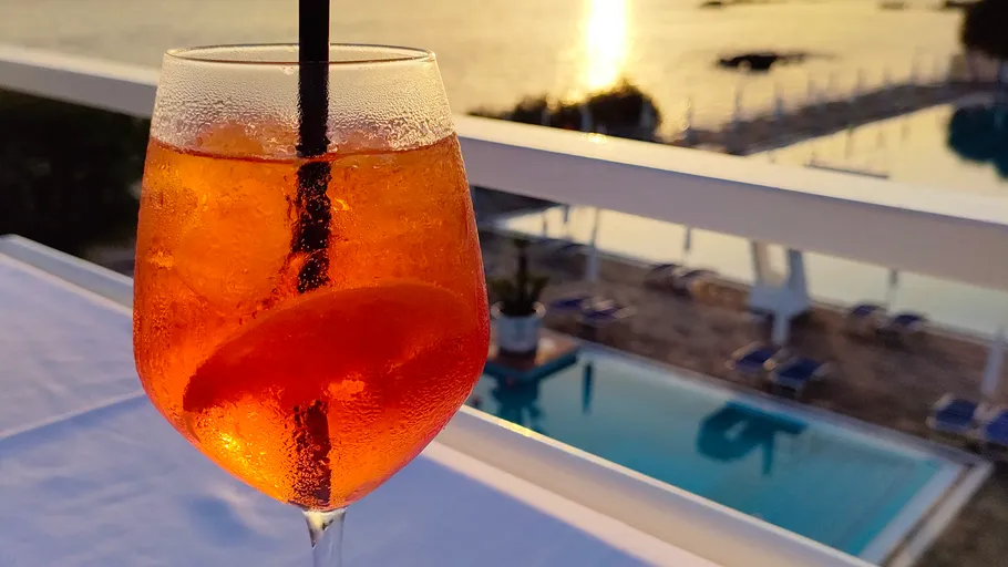Orange cocktail with straw by sunset pool.