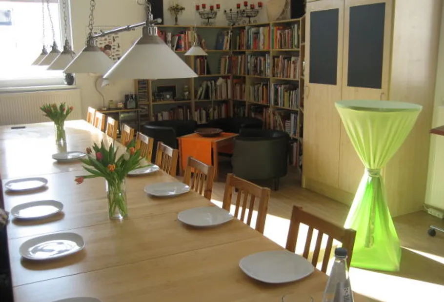 Dining table with plates and flowers, bookshelves behind.