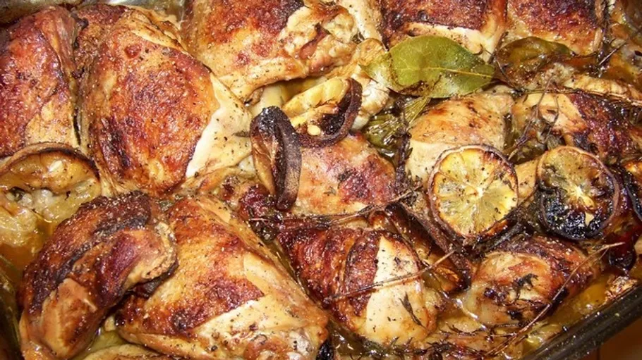 Roasted chicken with lemons and herbs in dish.