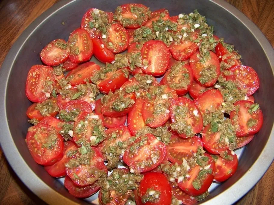 Halbierte Tomaten mit Kräutern in einer Backform.