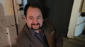 Smiling man in brown jacket indoors.