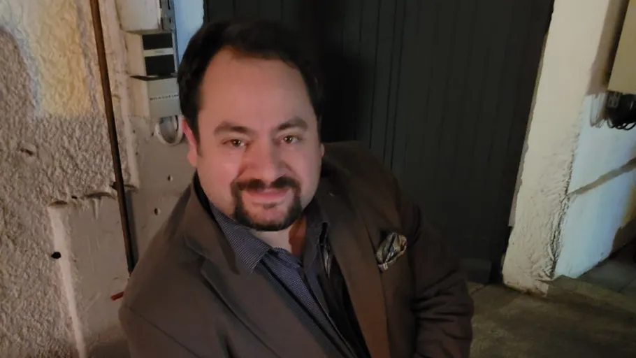 Smiling man in brown jacket indoors.