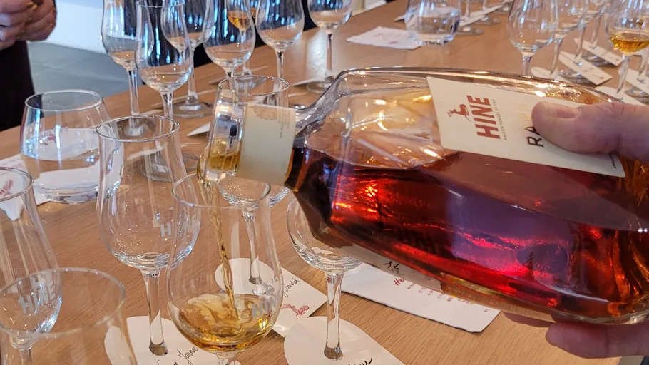 Person pouring brandy into a glass, wooden table.