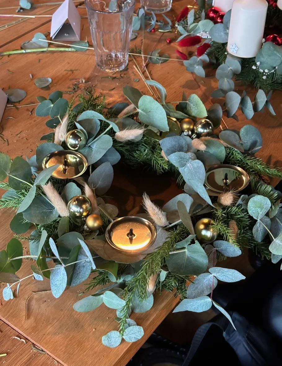 Decorative wreath with greenery and candles on table.