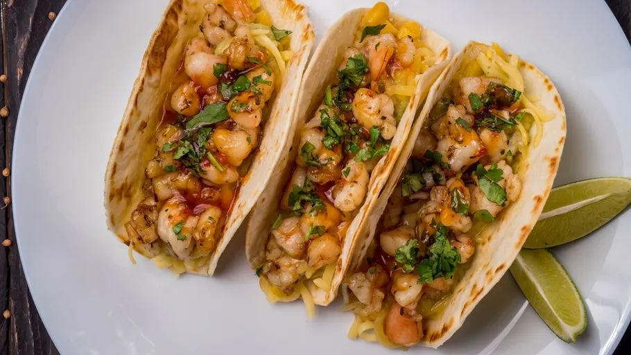 Three shrimp tacos with lime wedges.