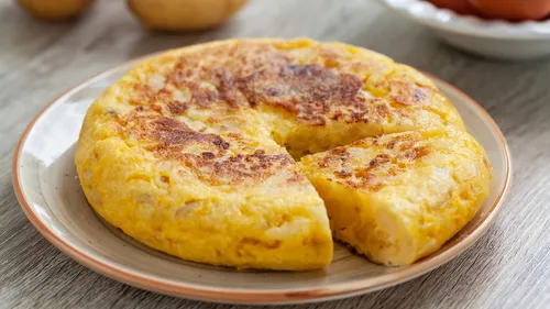 Spanish omelette with a slice removed on plate.