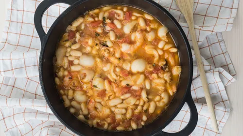 Pot of beans stew on checkered cloth.