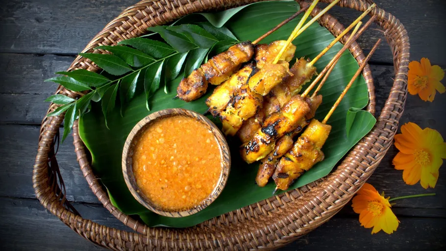 Grilled satay sticks with sauce in basket.