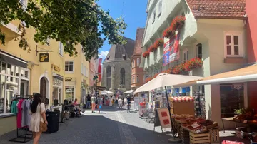 Menschen spazieren auf Kopfsteinpflasterstraße, Geschäfte herum.