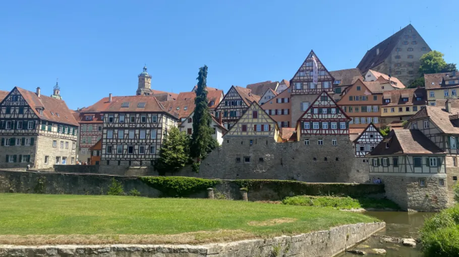 Half-timbered houses by a riverbank under blue sky.