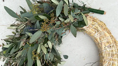 Decorative wreath with green leaves on straw base.