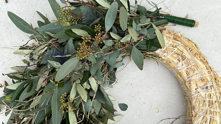 Decorative wreath with green leaves on straw base.