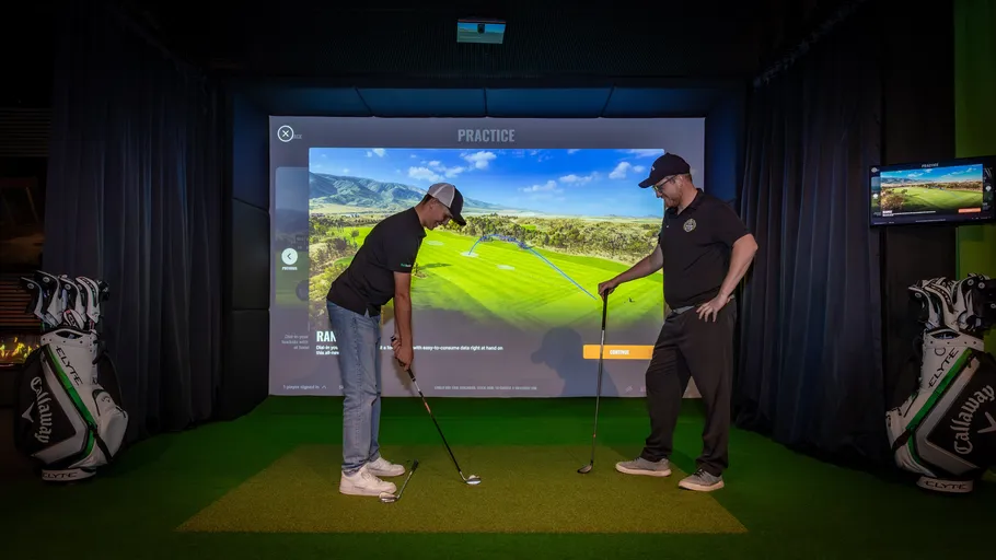 Zwei Personen spielen Golfsimulation drinnen.