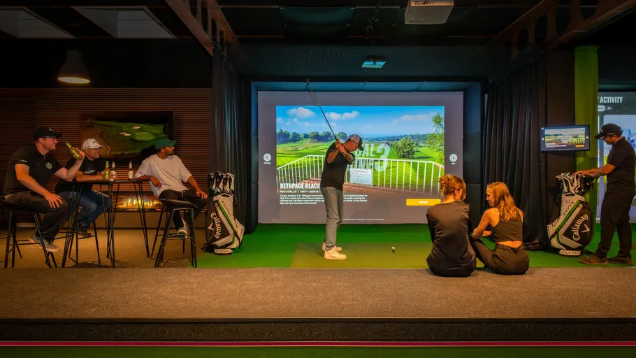 Gruppe schaut Mann beim Indoor-Golf zu.