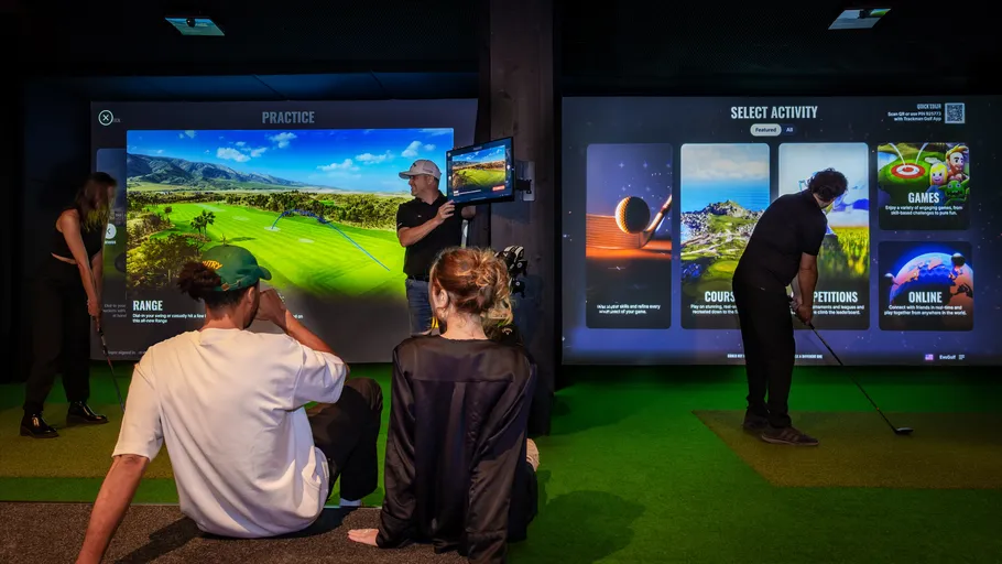 People playing virtual golf in an indoor simulator.