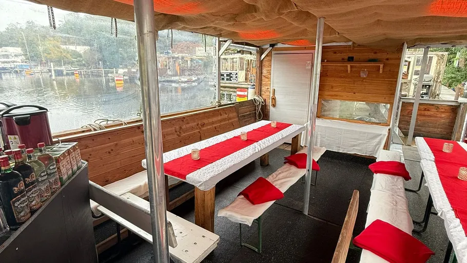 Überdachtes Bootinnenraum mit Tischen, roter Dekor.