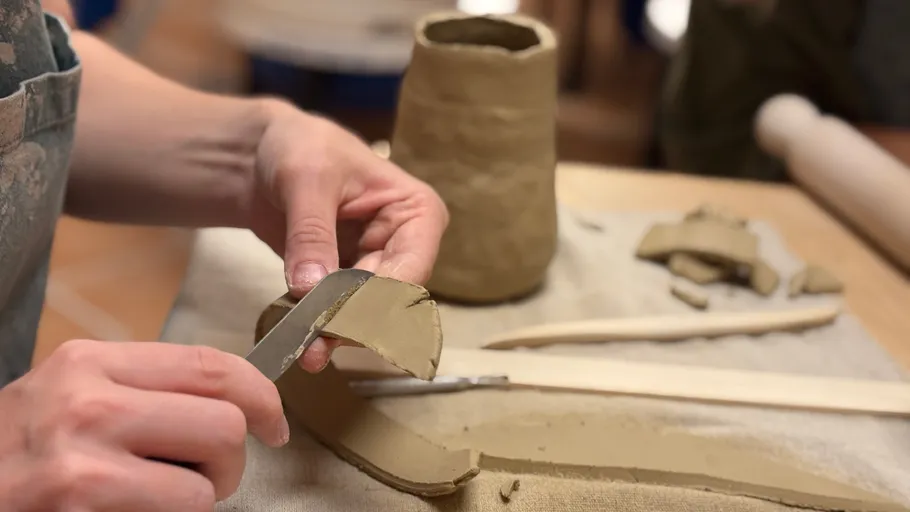 Hands shaping clay with a tool on table.