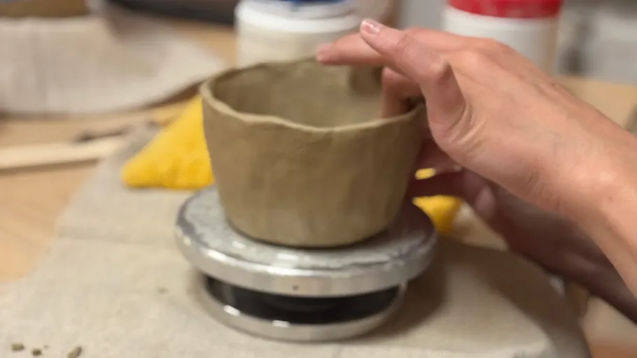 Hands shaping clay bowl on potter's wheel.