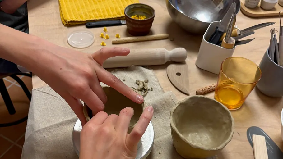 Hands shaping clay bowls on table.
