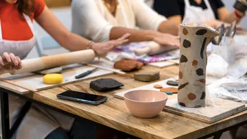 People crafting pottery at a wooden table.