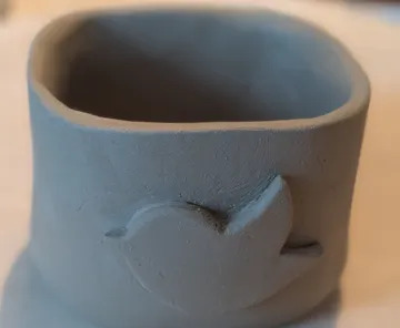 Clay cup with bird design, on table.