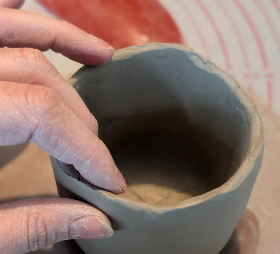 Hand formt Tontopf auf Arbeitsfläche.