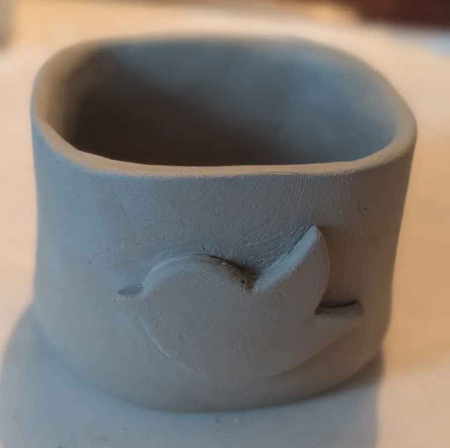 Tonebecher mit Vogelmotiv auf Tisch.