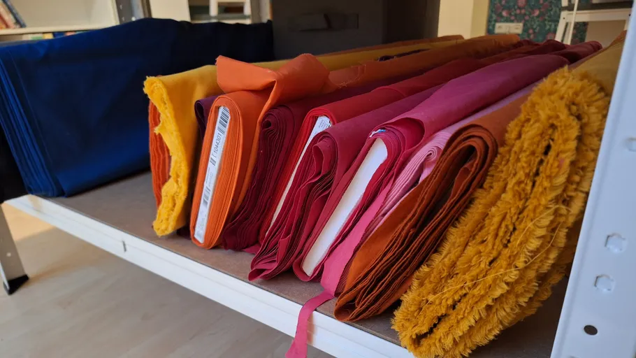 Colorful fabric rolls stacked on shelf.