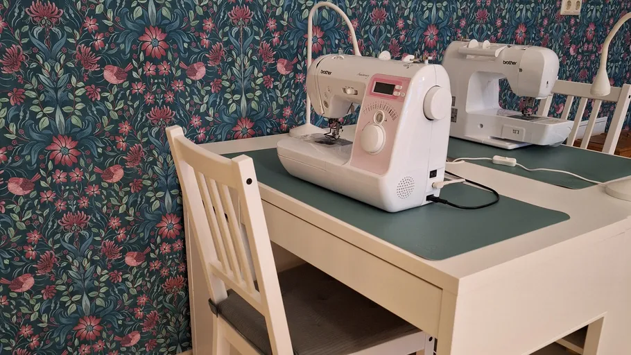 Sewing machines on white table in floral room.