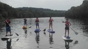 Fünf Personen beim Stand-up-Paddeln auf einem Fluss.
