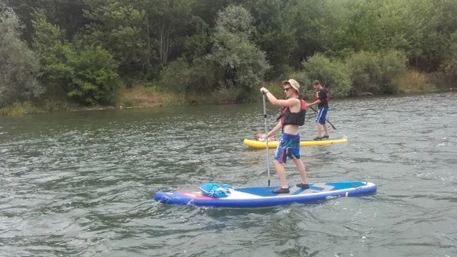 Zwei Personen paddleboarden auf einem Fluss, umgeben von Bäumen.