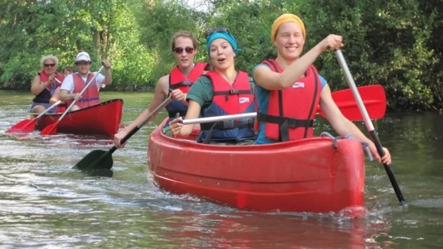 Gruppe paddelt in roten Kanus auf einem Fluss.