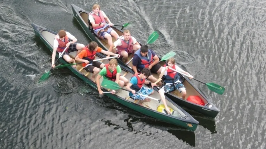 Drei Kanus mit Menschen paddeln auf Wasser.